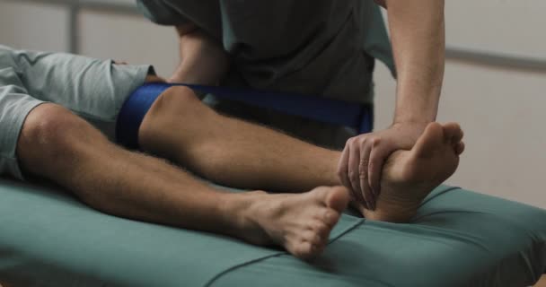 Physiotherapeutin bei der Arbeit mit einem männlichen Patienten. Reha-Training für gebrochenen Beinpatienten auf dem Krankenhausbett — Stockvideo