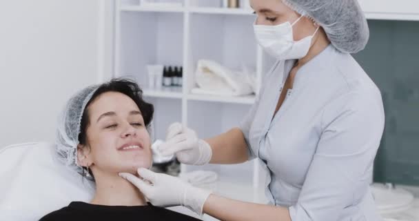 Mujer joven sentada en silla mientras visita a una hermosa cosmetóloga. Preparación para procedimientos cosméticos, inyección, ampliación de los labios — Vídeos de Stock