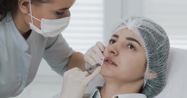 Увеличение губ. Врач-косметолог проводит процедуру наращивания губ красивой женщины в салоне красоты. Концепция инъекции косметической красоты — стоковое видео