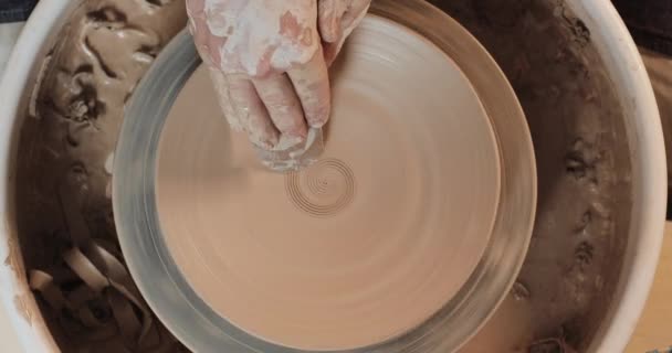 手は、粘土板のレリーフを形作る、プロのツールで陶器のホイールに取り組んでいます。トップビュー。ポッターは仕事で、近づいている。ハンドメイド、クラフト。白い粘土 — ストック動画