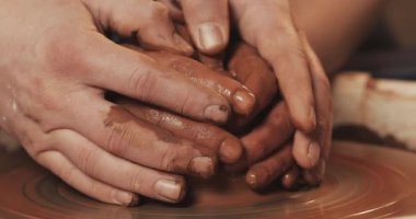 Çiftin elleri çömlekçi tekerleğinde bir çömlek kil oluşturur. Bir erkek el bir kadın elleri kil şekli şekillendirmek yardımcı olur. Yakın çekim.