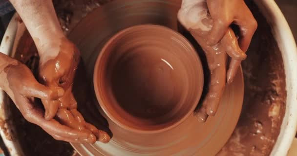 Handen van een paar vormen een pot klei op een Potters wiel. Een vrouwelijke hand helpt een Mans handen vorm een klei vorm. Top View. — Stockvideo