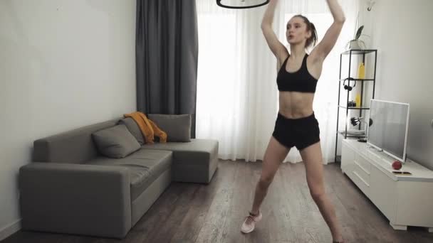 Mladá fitness žena trénuje ranní cvičení v domácím interiéru. Zpomal. Boční sedlo Hop cvičení. Zdravý a sportovní životní styl. — Stock video