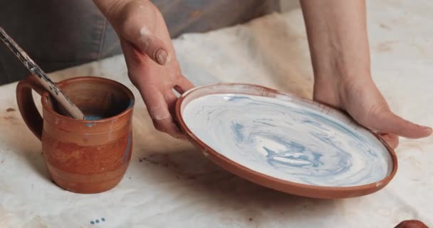 熟练的陶艺家釉覆盖着红粘土的盘子。特写。过程。陶瓷车间. — 图库视频影像