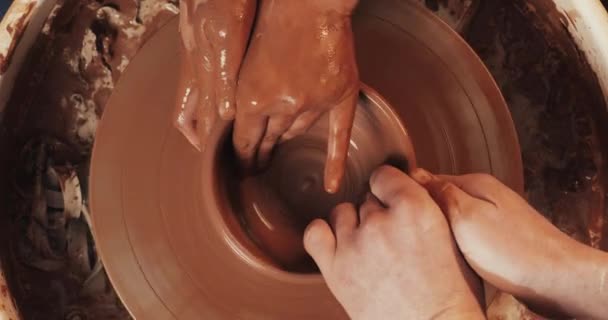 De handen van een man en een vrouw in klei op een Potters wiel schimmel een vaas. De Potter werkt in een pottenbakkerij met klei. — Stockvideo