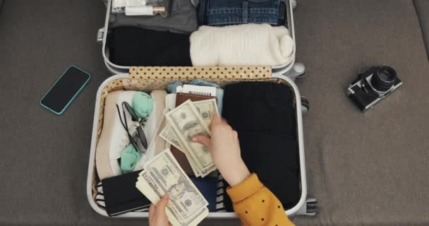 Dinero para viajar. Manos de mujer contando billetes de dólar en el fondo de la maleta. La chica se va de viaje. La maleta con las cosas . — Vídeo de stock