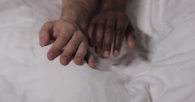 Çok ırklı çift, yatakta birlikte yatarken el lerine tutunuyor. Yakın çekim.