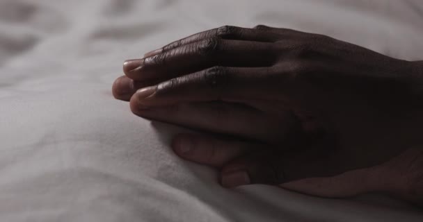 Ein verliebtes multiethnisches Paar, das zusammen im Bett liegt. Nahaufnahme. Männerhand liegt auf einem Bett, Frauenhand streichelt es und greift. — Stockvideo