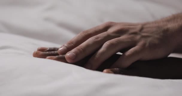 Birbirine aşık çok ırklı çift yatakta yatıyor. Yakından kapatın. Kadın eli bir yatakta yatıyor, erkek eli okşuyor ve tutuyor. — Stok video