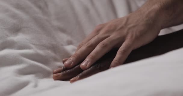 Birbirine aşık çok ırklı çift yatakta yatıyor. Yakından kapatın. Kadın eli bir yatakta yatıyor, erkek eli okşuyor ve tutuyor. — Stok video