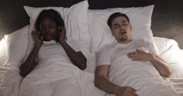 一緒にベッドに横たわっている多民族のカップル。女性はベッドでいびきをかく彼女のパートナーに苦しんでいます。カップルのライフスタイルと人々のヘルスケアの概念. — ストック動画
