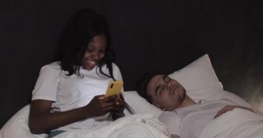 Mutlu çok ırklı çift battaniye altında gece yatakta yatıyordu. Genç kocası uyku, eşi yakışıklı mesajlaşma ve cep telefonu üzerinden online hile yaparken.
