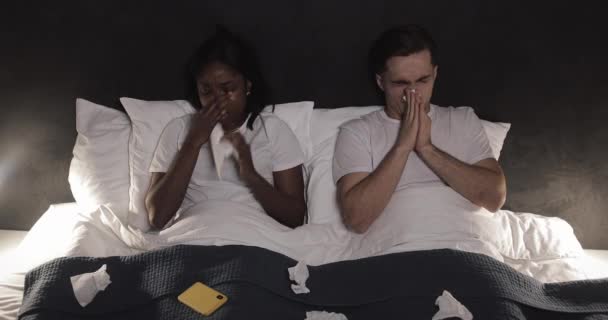 Krankes multiethnisches Paar, das im Bett liegend die Nase pustet. Unwohlfühlkonzept. — Stockvideo