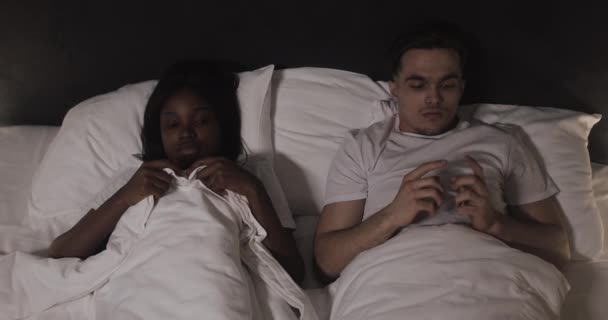 Geceleri yatakta yatan çok ırklı genç bir çift. Yatağa girmeden önce utangaç ve utangaç genç bir çift.. — Stok video