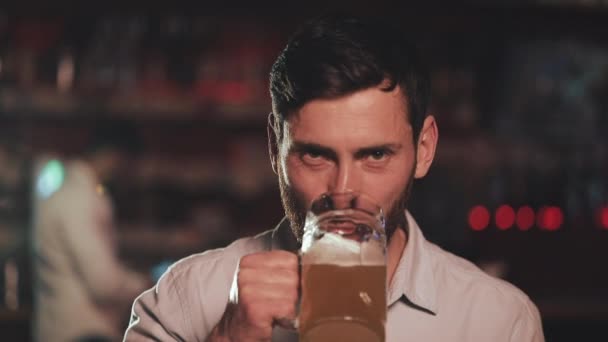 Porträt eines attraktiven Mannes, der Bier trinkt und in einer Bar oder Bierstube in die Kamera blickt. Konzept von Jugend, Freundschaft und Ruhe. — Stockvideo