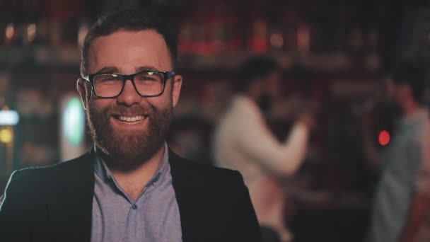 Portréja mosolyogva vonzó ember visel szemüveg nézi kamera egy bárban vagy a sör pub. Az ifjúság, a barátság és a pihenés fogalma. — Stock videók