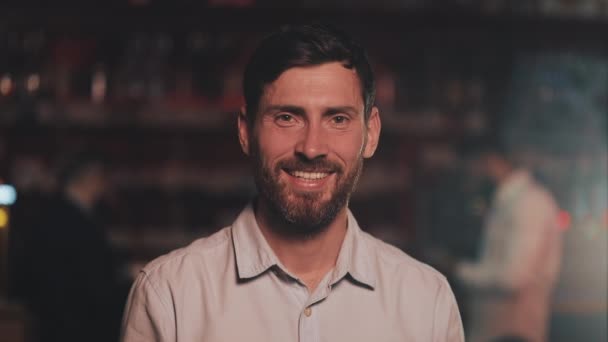 Portret van glimlachende aantrekkelijke man die naar de camera kijkt in een bar of bierpub. Begrip jeugd, vriendschap en rust. — Stockvideo