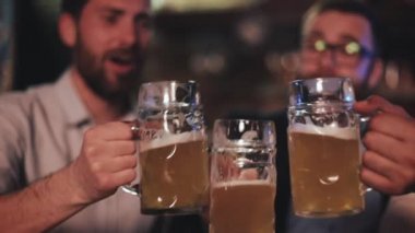 Üç eski arkadaş barda bira ile gözlüklerini kucaklayarak. Yakın çekim, yavaş hareket. Kutlama bira Cheers kavramı.