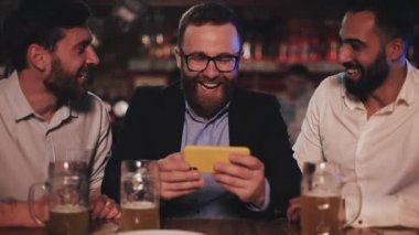 Üç eski arkadaş spor bar akıllı telefon ve içme taslak bira video izliyor. Arkadaşlar gülmek ve bira pub haberleri tartışmak.