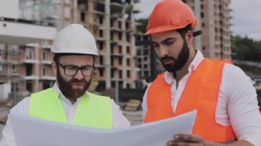 Mimar uzman mühendisleri konuşan ve tasarım planı inşaat alanında ayakta analiz. Meslekler, inşaat, işçiler, mimar konsepti. Yavaş hareket.