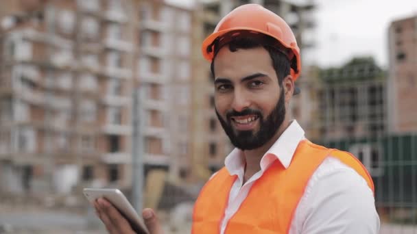 Portret van bouwvakker op bouwplaats met Tablet die naar de camera kijkt. Close-up. Beroepen, bouw, werknemers, architect concept. — Stockvideo