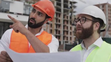 Mimar uzman mühendisleri konuşan ve tasarım planı inşaat alanında ayakta analiz. Meslekler, inşaat, işçiler, mimar konsepti. Yavaş hareket.