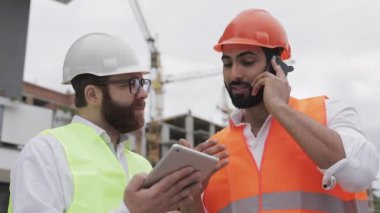 Mühendis inşaat yerinde cep telefonu konuşuyor ve işçi çalışmalarını kontrol eder. Akıllı telefonda Builder görüşmeleri. Bitmemiş proje.