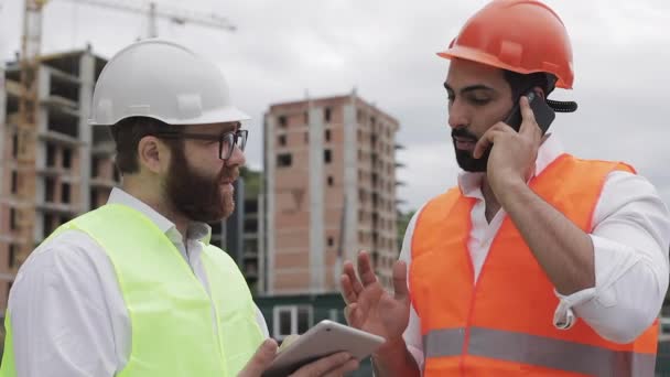 Ingenjör talar på mobil telefon på bygg arbets platsen och kontrollerar arbets tagarens arbete. Builder pratar på smartphone. Oavslutat projekt. — Stockvideo