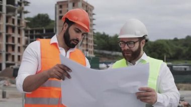 Mimar uzman mühendisleri konuşan ve tasarım planı inşaat alanında ayakta analiz. Meslekler, inşaat, işçiler, mimar konsepti. Yavaş hareket.