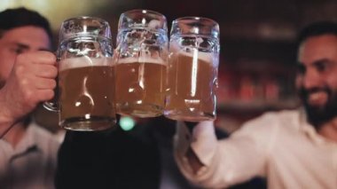 Üç eski arkadaş barda bira ile gözlüklerini kucaklayarak. Yakın çekim, yavaş hareket. Kutlama bira Cheers kavramı.