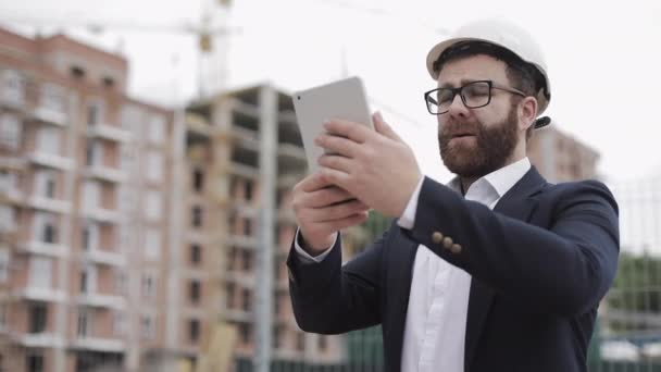 Jovem arquiteto barbudo no canteiro de obras tirando foto com tablet. Vestiu-se de fato de negócios . — Vídeo de Stock