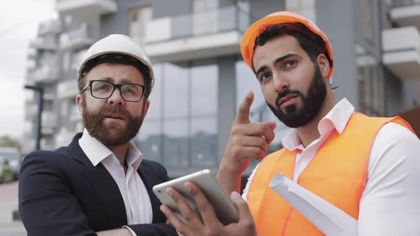 Construction Manager en architect man bespreken het bouwplan van het moderne Business Center. Zij controleert het werk met een Tablet. Buiten. — Stockvideo