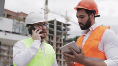 Mühendis inşaat yerinde cep telefonu konuşuyor ve işçi çalışmalarını kontrol eder. Akıllı telefonda Builder görüşmeleri. Bitmemiş proje.