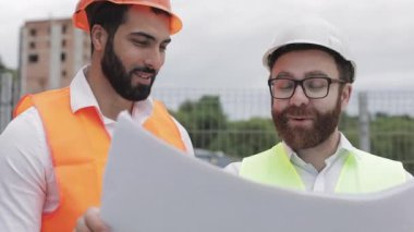 İnşaat bölgesinde mimar ile gülen erkek inşaat mühendisi tartışma veya Highrise binanın bina sitesi. Onların ellerinde inşaat çizimleri tutuyor.