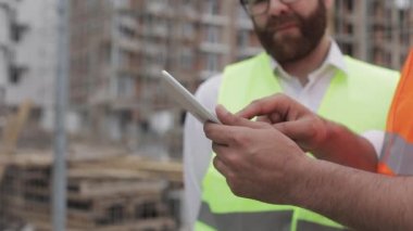 Şantiye yakın tablet kullanarak mimar elleri yakın. Kurucu ve mimar adam modern iş merkezinin inşaat planını tartışıyor.