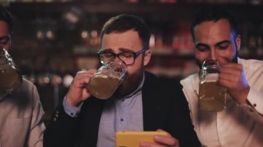 Üç eski arkadaş spor bar akıllı telefon ve içme taslak bira video izliyor. Arkadaşlar gülmek ve bira pub haberleri tartışmak.
