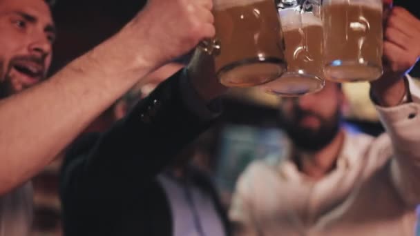3人の古い友人がパブでビールでグラスを鳴らしている。クローズアップ、スローモーション。お祝いのビールの乾杯の概念. — ストック動画