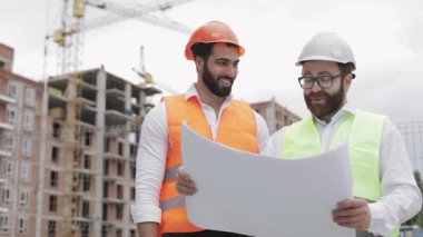 İnşaat bölgesinde mimar ile gülen erkek inşaat mühendisi tartışma veya Highrise binanın bina sitesi. Onların ellerinde inşaat çizimleri tutuyor.