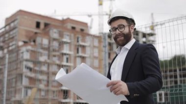 Kamera bakarak bina site üzerinde yakışıklı genç mühendis portresi. İnşaat projesi ile kurucu modern bir binanın arka planda duruyor. Yavaş hareket.