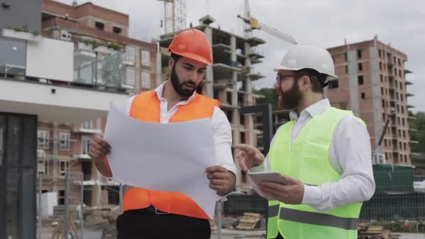 Budowanie kompleksu mieszkaniowego lub centrum biznesowego. Zespół inżynierów mężczyzn z tabletem i rysunek analizując plany budowniczych działalności pracy. — Wideo stockowe