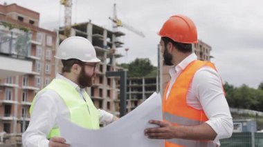 Yüksek katlı binanın şantiye veya şantiyemimar ile erkek inşaat mühendisi tartışma. Ellerinde inşaat çizimleri tutuyorlar..