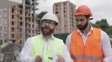 İnşaatçı ve mimar adam inşaat alanı yakınında yürüyen modern iş merkezinin inşaat planı tartışıyorlar. Onlar mimari taslak ile iş kontrol.