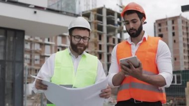 İnşaatçı ve mimar adam inşaat alanı yakınında yürüyen modern iş merkezinin inşaat planı tartışıyorlar. Onlar bir tablet ve mimari taslak ile çalışma kontrol.