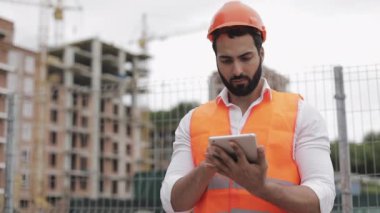 Mimar adam inşaat yerinde tablet ile ayakta ve şeması proje planı analiz. Dışarıda, yavaş hareket.