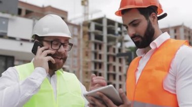 Mutlu mühendis şantiyede cep telefonuyla konuşuyor ve işçinin çalışmalarını kontrol ediyor. Akıllı telefonda oluşturucu konuşuyor. İnşaat aşamasının kontrol edilmesi