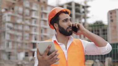 Müfettiş bina yönetici mühendisi akıllı telefonda konuşurken ve inşaat sitesi arka planda tablet ayakta üzerinde çalışıyor. Meslek konsepti.