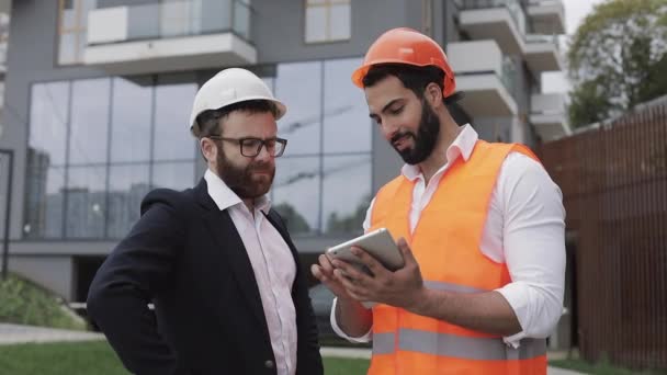 Direttore edile e architetto uomo stanno discutendo il piano di costruzione del moderno centro commerciale. Controllano il lavoro con un tablet. Fuori. . — Video Stock