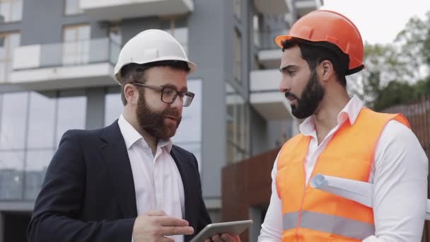 Bauleiter und Architekt besprechen den Bauplan für das moderne Geschäftszentrum. Sie prüfen die Arbeit mit einem Tablet. Außen. — Stockvideo