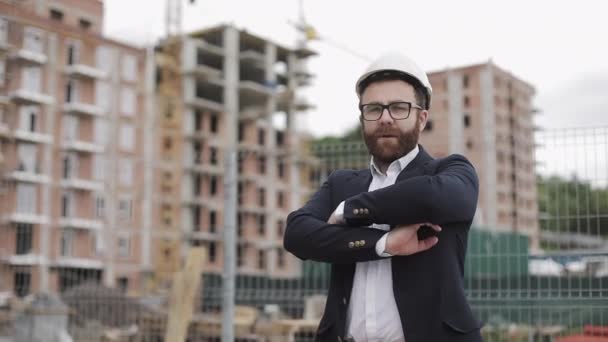 Portrait of architect man in business suit standing on the construction site with crossed hands looking at the camera. Outside, slow motion. — Stock Video