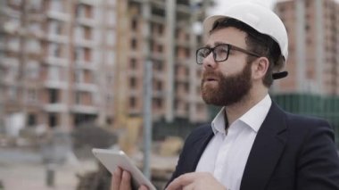 Mimar adam şantiye ve analiz şeması proje planı üzerinde tablet ile ayakta iş elbisesi giyiyor. Dış, yavaş çekim.